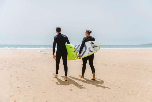 two people standing on the beach holding their surfboards at Radisson Blu Resort Taghazout Bay Surf Village in Taghazout