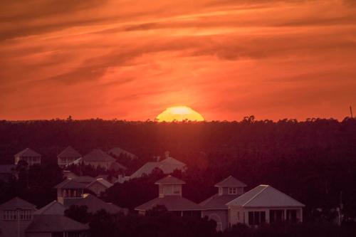 a sunset with the sun in the sky over houses at Plantation Dunes #5101 in Gulf Shores