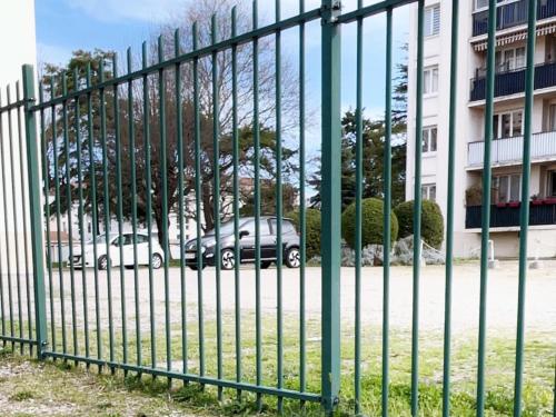 a green fence with cars parked in a parking lot at Appartement 5 Lits, tout équipé, WiFi, NetfliX in Vaulx-en-Velin
