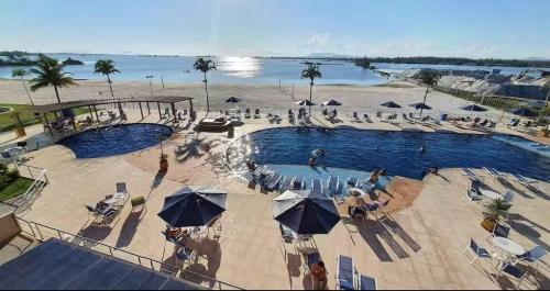 a swimming pool with umbrellas and people on a beach at Golden Lake Residence Apart Hotel in Arraial do Cabo