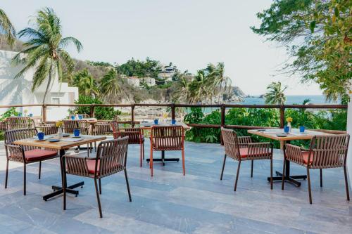 a patio with tables and chairs and a view of the ocean at Camino Real Zaashila Huatulco in Santa Cruz Huatulco