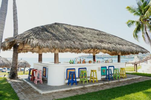 a beach bar with colorful chairs and a straw umbrella at Camino Real Zaashila Huatulco in Santa Cruz Huatulco