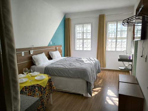 a bedroom with a bed with a table and two windows at Suites Duarte in Ouro Preto