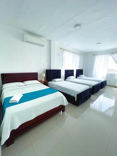 three beds in a room with white walls and windows at HOSTAL PIAZZOLLA in Manta