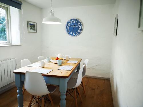 a dining room table with white chairs and a clock on the wall at Maple Barn in Porthtowan