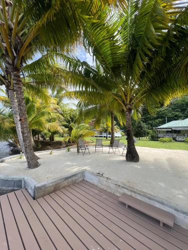a wooden deck with two palm trees and benches at Fare Mama Rota - au bord de l'océan in Taputapuapea