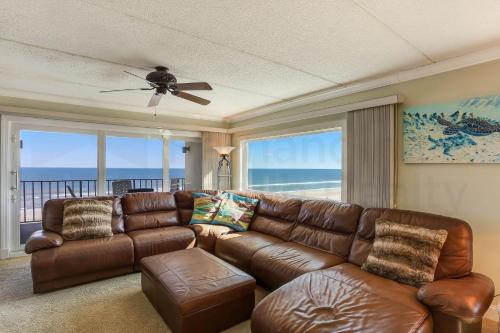 a living room with a brown leather couch and windows at Amelia South - B7 in Fernandina Beach