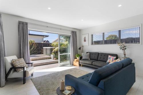 a living room with a blue couch and a window at Sun and Surf Retreat - Papamoa Beach Holiday Home in Papamoa