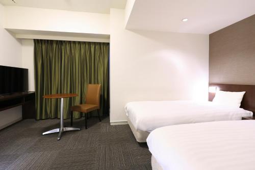 a hotel room with two beds and a table and a tv at Dormy Inn Matsumoto in Matsumoto