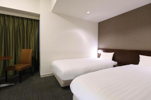 a hotel room with two beds and a table and chair at Dormy Inn Matsumoto in Matsumoto