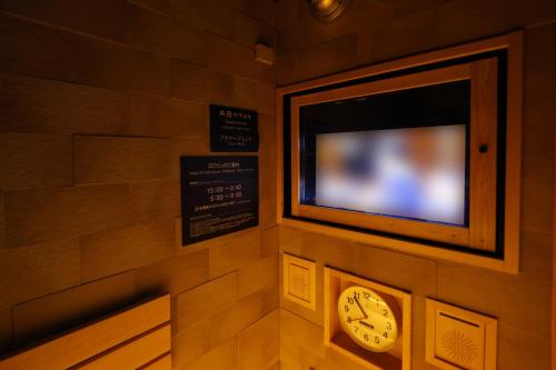 a clock on a wall with a tv on it at Dormy Inn Matsumoto in Matsumoto