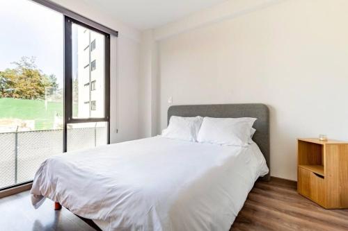 a white bedroom with a bed and a large window at Moderno Loft Totalmente Equipado in Lomas de Angelopolis