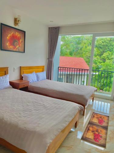 two beds in a room with a large window at Hotel & Homestay Long Vũ Măng Đen in Kon Tum