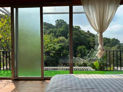 a bedroom with a large window looking out at a garden at Hotel & Homestay Long Vũ Măng Đen in Kon Tum