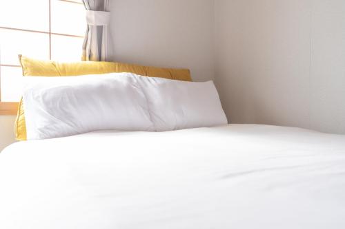 a bed with white sheets and a yellow pillow at +C FURANO in Furano