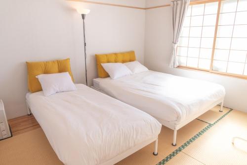 two beds in a small room with a window at +C FURANO in Furano