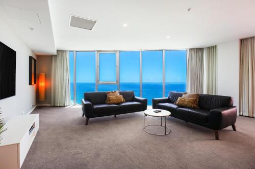 a living room with two black couches and the ocean at Number 1 H Residences - WiFi, Parking & More by Gold Coast Holidays in Gold Coast