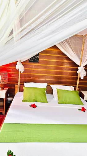 a bedroom with a white bed with green pillows at Bungalows des tropiques in Nosy Be