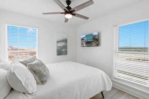 a white bedroom with a ceiling fan and two windows at White Sand Beachfront Paradise in Gulf Shores