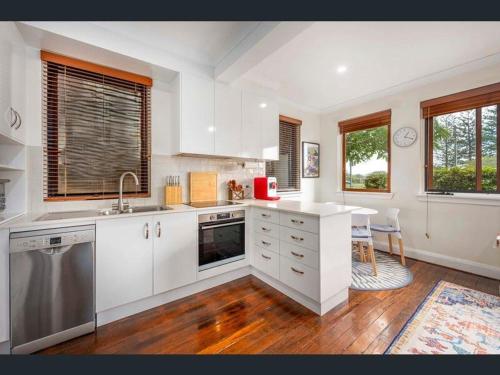 a kitchen with white cabinets and a table and two windows at River View - Modern Living in a Vintage Apartment in Brunswick Heads