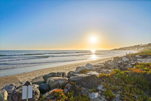 a beach with rocks and the sun rising over the ocean at The Surf Lodge Villa in Malibu