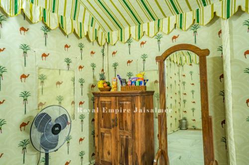 a bedroom with palm trees wallpaper and a fan at Royal Empire Camp & Resort Jaisalmer in Sām