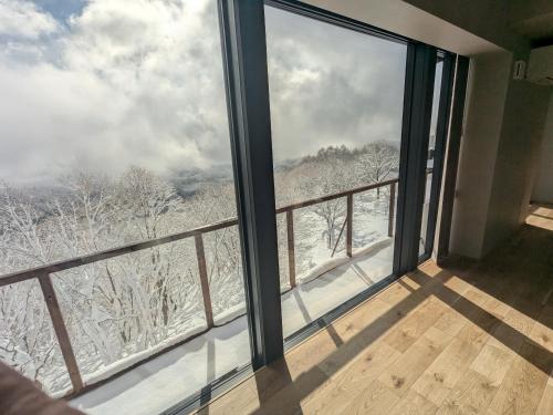 a room with a large window with snow covered trees at Fujio Pension Madarao Apartment Hotel & Restaurant in Iiyama
