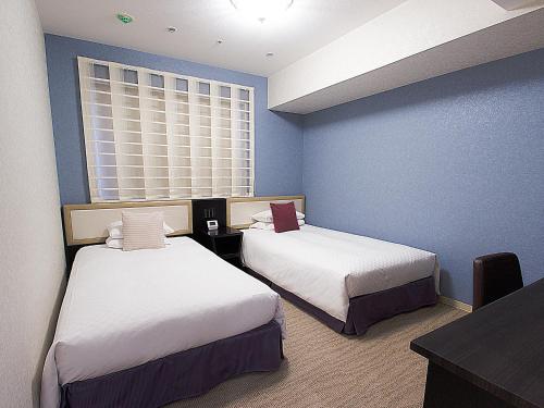 a room with two beds and a table and a window at Hearton Hotel Kita Umeda in Osaka