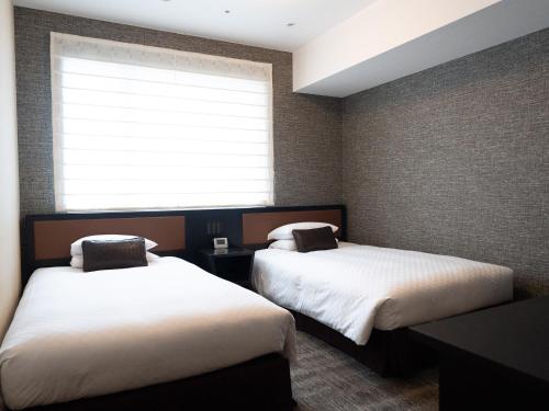 two beds in a room with a window at Hearton Hotel Kita Umeda in Osaka