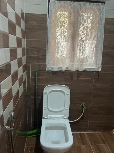 a bathroom with a toilet with a window and a curtain at Amazing Homestay in Guwahati