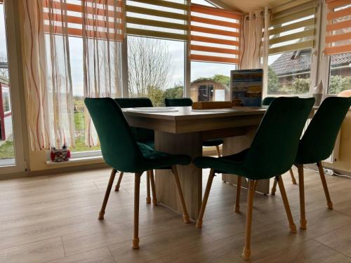 a dining room table with green chairs and windows at Ferienhaus An der Riede in Bedekaspel