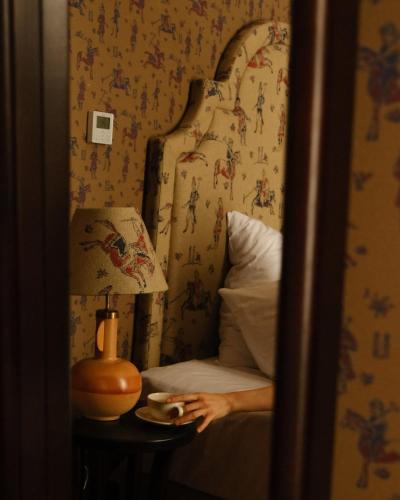 a person sitting on a bed with a cup on a table at Communal Hotel Kutaisi in Kutaisi