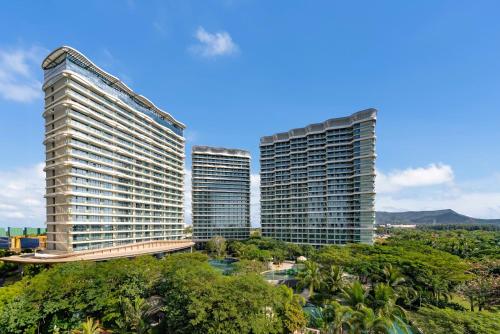 three tall buildings in a city with trees at Puhai Sea View Apt by Hailan Tour at Sanya Yazhou Bay#only 100 meters to Beach and Sea Swimming Area in Sanya