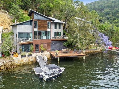 a house on a dock with a boat in the water at Berowra Waters Glass House in Berrilee