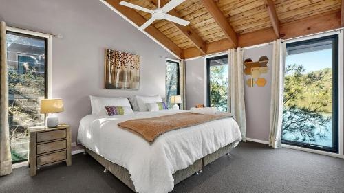 una camera da letto con un letto grande e grandi finestre di Berowra Waters Glass House a Berrilee