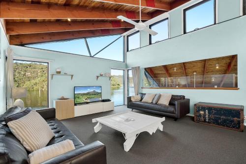 a living room with couches and a tv and a table at Berowra Waters Glass House in Berrilee