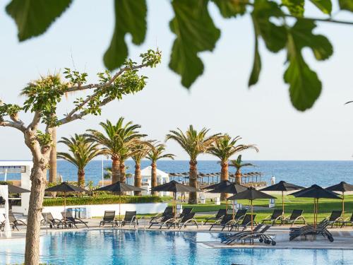a swimming pool with chairs and umbrellas and the ocean at Grecotel Creta Palace in Rethymno Town