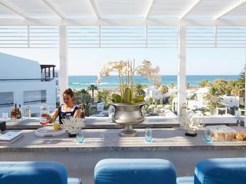 a woman sitting at a table in front of the beach at Grecotel Creta Palace in Rethymno Town