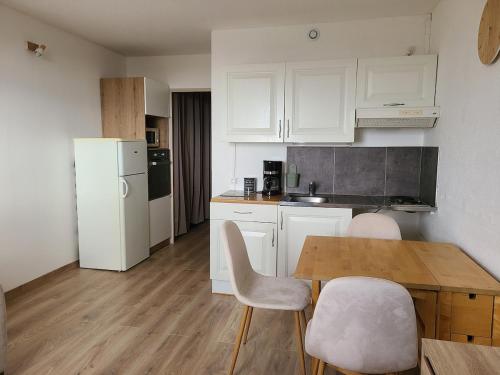 une cuisine avec des armoires blanches et une table et des chaises en bois dans l'établissement Appartement à la plage, vue sur la mer, à Calais