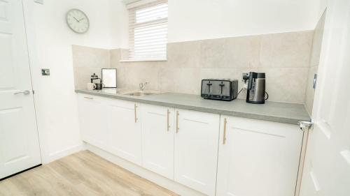 a kitchen with white cabinets and a clock on the wall at The Cheltenham Suites - Collection of Luxury Flats in Cheltenham
