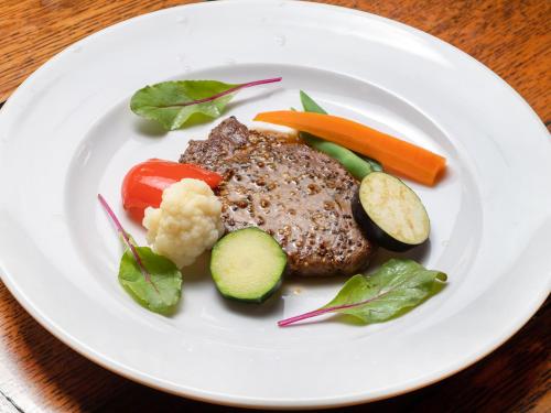 a white plate with meat and vegetables on a table at Gasthof Ami in Nikko