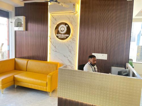 Un hombre sentado en un escritorio en una sala de espera. en Hotel Mb Nirala Shyam, en Khātu