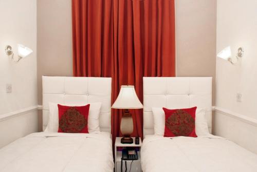 two beds in a room with red curtains at Classic Hyde Park Hotel in London