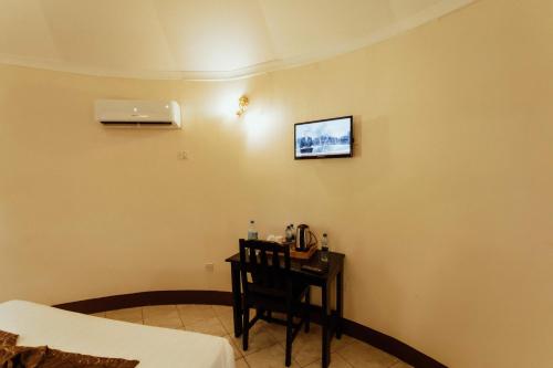 a room with a bed and a table with a television on the wall at Keys Hotel in Moshi