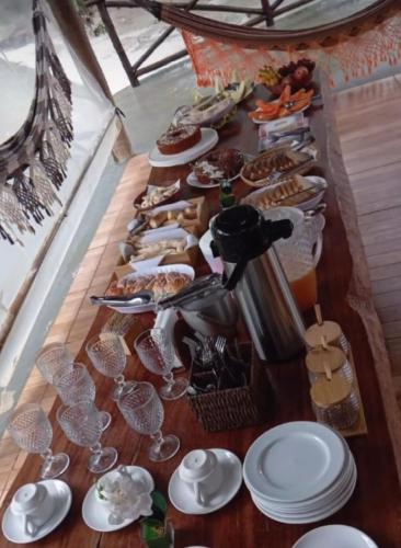 a long table with plates and glasses and food at Chalés Riacho da Serra Capitólio in Guapé