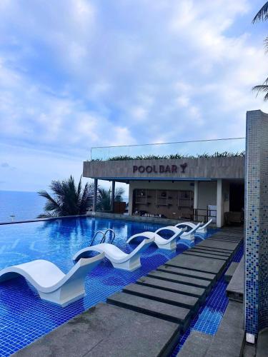 a pool bar with white lounge chairs next to the ocean at Apec Mandala Mũi Né Sun Sea Condotel in Mui Ne