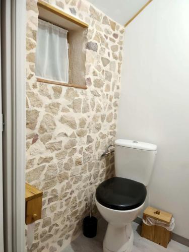 La salle de bains est pourvue de toilettes noires et d'un mur en pierre. dans l'établissement Gîte rural au Bois des Riots, à Montillot
