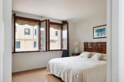 a white bedroom with a bed and two windows at Palazzo Contarini Della Porta Di Ferro in Venice