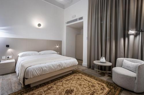a white bedroom with a bed and a chair at Old Theatre Suites - Montecristo in Valletta