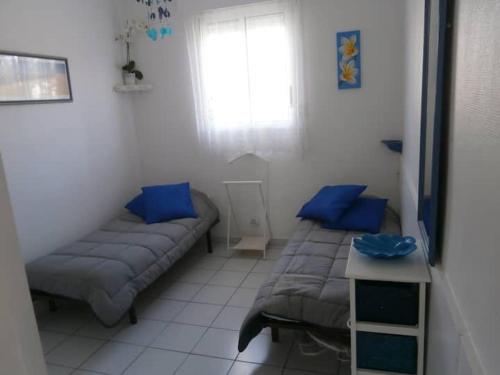 Cette chambre comprend 2 lits et une fenêtre avec des oreillers bleus. dans l'établissement APPART BISCA plage, à Biscarrosse